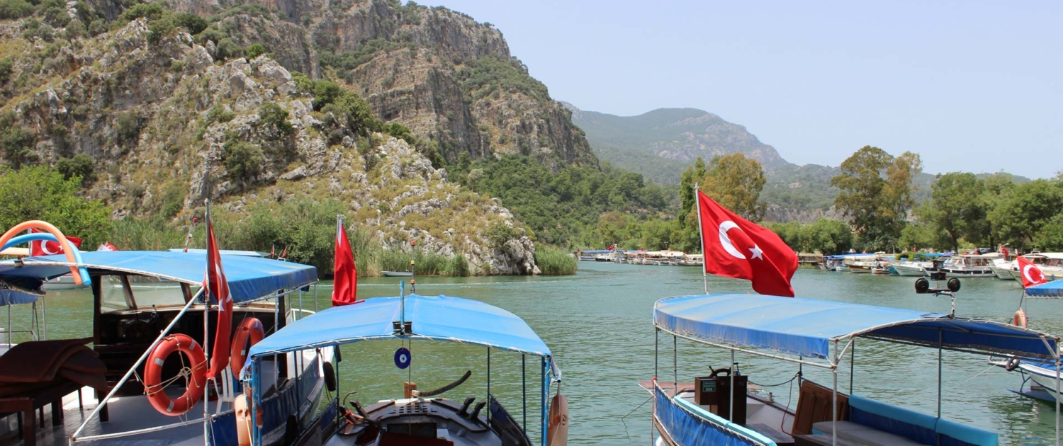 Traditionelle türkische Boote mit türkischen Flaggen auf dem Dalyan-Fluss, umgeben von malerischen Hügeln.