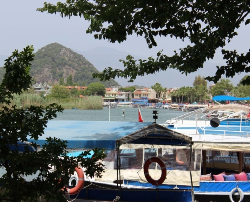 Boote im Hafen von Dalyan, umgeben von grüner Natur und türkischen Flaggen.
