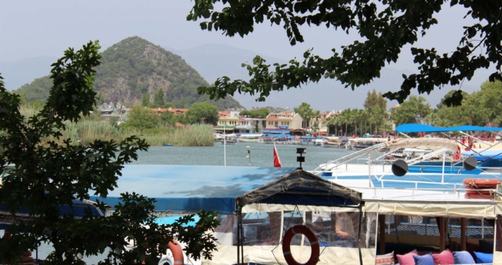 Boote im Hafen von Dalyan, umgeben von grüner Natur und türkischen Flaggen.